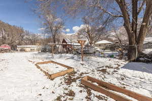 Yard layered in snow featuring a playground and a vegetable garden