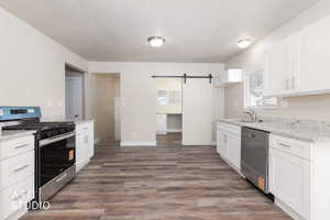 Kitchen with a barn door, stainless steel appliances, white cabinetry, and dark wood-type flooring
