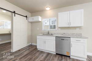 Kitchen featuring stainless steel dishwasher, white cabinetry, light stone counters, a barn door, and dark wood-style flooring