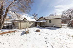 Snow covered rear of property with a fenced backyard, an outdoor fire pit, an outdoor structure, and a gate
