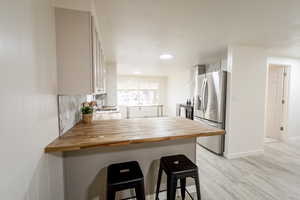 Kitchen featuring a breakfast bar area, a peninsula, stainless steel fridge with ice dispenser, light wood-style floors, and decorative backsplash