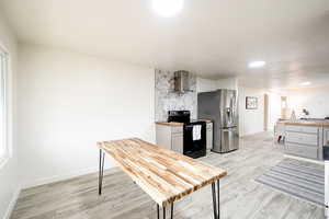Kitchen featuring butcher block countertops, light wood-style floors, black electric range oven, decorative backsplash, and stainless steel refrigerator with ice dispenser
