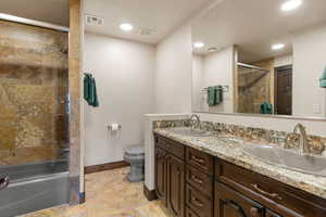 Bathroom with double vanity, bath / shower combo with glass door, and light stone finish flooring