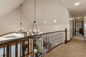 Corridor with light carpet, hanging lights, and lofted ceiling