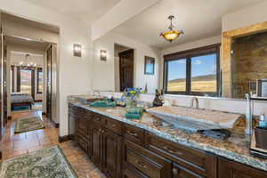 Bathroom featuring stone tile flooring, double vanity, plenty of natural light, and connected bathroom