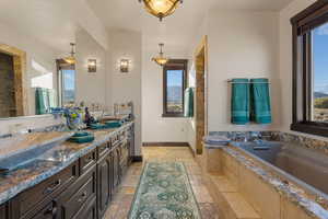 Full bathroom featuring stone tile floors, double vanity, a garden tub, a shower, and a mountain view