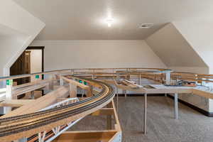 Misc room with carpet flooring, a textured ceiling, and an upstairs landing