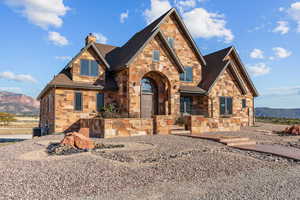 View of front facade featuring stone siding, a mountain view, a chimney, and roof with shingles