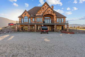 Back of property with a mountain view, stone siding, a chimney, and roof with shingles