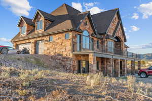View of home's exterior featuring stone siding, roof with shingles, a balcony, and a garage