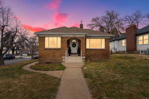 Bungalow-style home with a lawn, a chimney, brick siding, and a shingled roof
