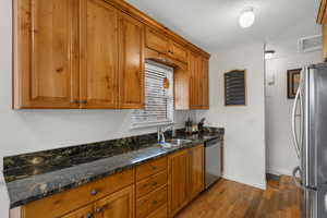 Kitchen featuring stainless steel appliances, wood finish cabinets, dark stone counters, and light wood-style flooring