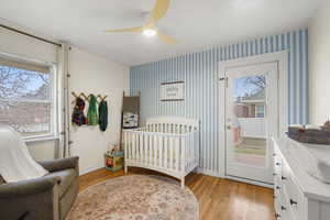 Bedroom featuring light wood-style floors, a ceiling fan, a nursery area, and wallpapered walls