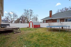 Fenced backyard featuring a storage unit, a deck, and a trampoline