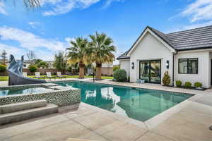 Integrated pool / hot tub featuring a water slide and a patio