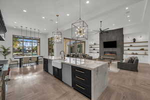 Kitchen with dark cabinets, light stone counters, parquet floors, open floor plan, and an island with sink
