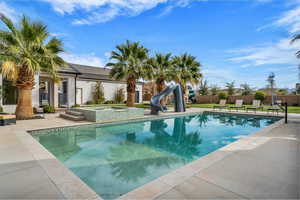 View of swimming pool with a water slide, patio surround, and an in-ground hot tub