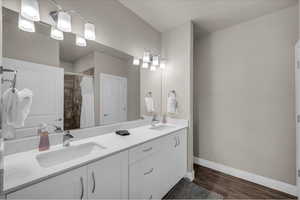 Bathroom with double vanity, a shower with shower curtain, and dark wood-style flooring