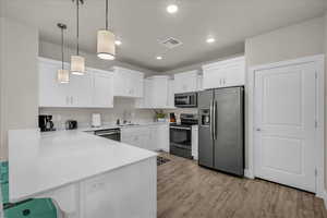 Kitchen with stainless steel appliances, decorative light fixtures, a peninsula, and white cabinetry