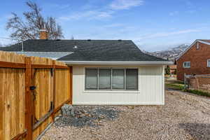 View of side of home featuring roof with shingles, a gate, a chimney, and a mountain view