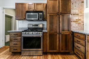 Kitchen featuring stainless steel appliances, light stone counters, light wood-style flooring, and tasteful backsplash