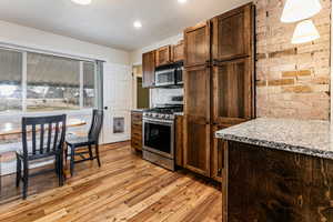 Kitchen with stainless steel appliances, light wood-style flooring, backsplash, light stone countertops, and recessed lighting