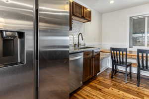 Kitchen featuring stainless steel appliances, dark wood finish cabinetry, dark wood-style flooring, light stone counters, and wainscoting