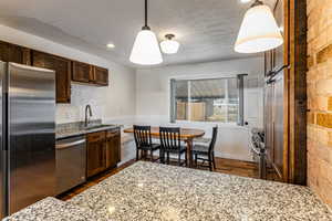 Kitchen with stainless steel appliances, decorative light fixtures, light stone counters, dark wood-type flooring, and dark wood finish cabinets