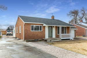 View of front of home featuring a shingled roof, brick siding, driveway, and a chimney