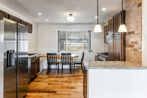Kitchen featuring stainless steel appliances, light wood-style floors, light stone countertops, a wainscoted wall, and dark wood finish cabinets