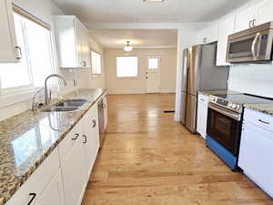 Kitchen with decorative backsplash, stainless steel appliances, white cabinetry, light stone counters, and light wood-style floors