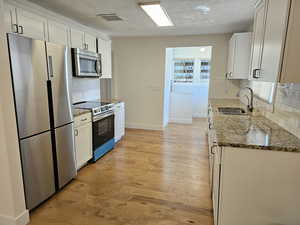 Kitchen with dark stone counters, stainless steel appliances, tasteful backsplash, light wood-style floors, and white cabinetry