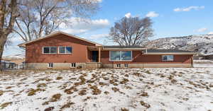 Snow covered back of property with brick siding and a mountain view