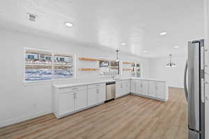 Kitchen with a peninsula, white cabinets, decorative light fixtures, light wood finished floors, and open shelves