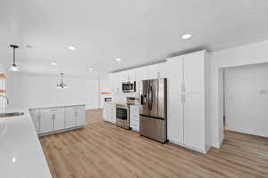 Kitchen with white cabinetry, stainless steel appliances, light wood-style floors, and light stone countertops