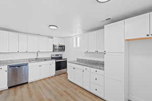 Kitchen featuring stainless steel appliances, white cabinets, light wood-style flooring, a textured ceiling, and light stone counters
