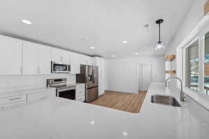 Kitchen featuring light stone counters, stainless steel appliances, light wood finished floors, white cabinetry, and hanging light fixtures