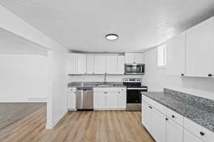 Kitchen featuring stainless steel appliances, white cabinets, light stone counters, a textured ceiling, and light wood-style floors