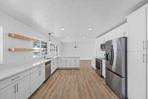 Kitchen with white cabinetry, stainless steel appliances, open shelves, decorative light fixtures, and light wood-style flooring