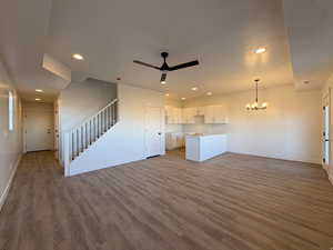 Unfurnished living room featuring a chandelier, ceiling fan, and dark wood-style floors