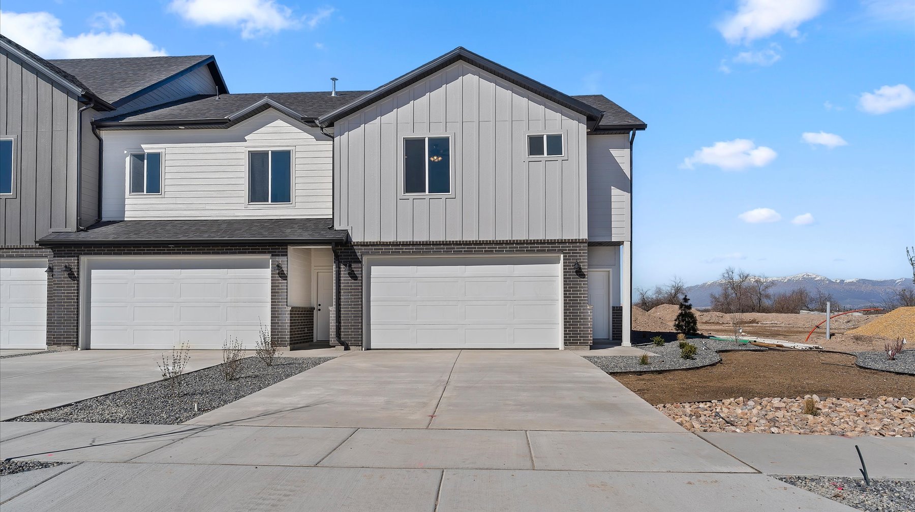 View of front facade with board and batten siding, an attached garage, driveway, brick siding, and a mountain view
