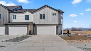 View of front facade with board and batten siding, an attached garage, driveway, brick siding, and a mountain view