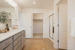 Bathroom featuring double vanity, light wood-type flooring, a stall shower, and a walk in closet
