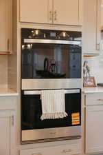 Kitchen view of tasteful backsplash, double oven, and white cabinetry