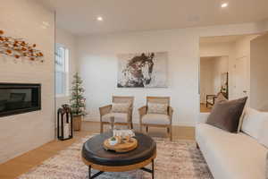 Living room with wood finished floors, a large fireplace, and recessed lighting