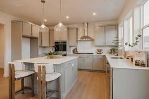 Kitchen featuring gray cabinetry, hanging light fixtures, light wood-type flooring, and a kitchen bar