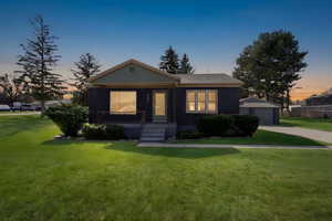 View of front of home featuring a front lawn, brick siding, a detached garage, a porch, and an outbuilding