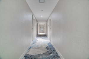 Hallway with carpet floors, recessed lighting, and a textured wall