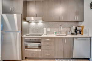 Kitchen featuring stainless steel appliances, modern cabinets, light stone countertops, and backsplash
