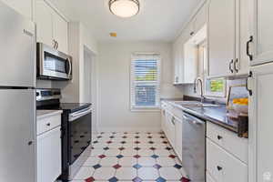 Kitchen with stainless steel appliances, dark countertops, white cabinets, light flooring, and tasteful backsplash